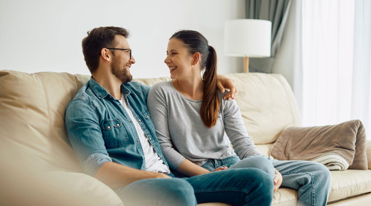 a happy couple sitting on settee smiling at each other